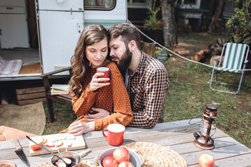 Wall Mural - Young beautiful loving couple travelling across country in the van. Millennial man and woman in a travel camper. Cozy atmosphere, vacations vibe. Drinking tea, playing guitar