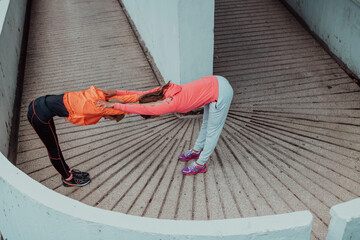 Wall Mural - Two women warming up together and preparing for a morning run in an urban environment. Selective focus 