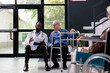 © DC Studio - Practitioner medic holding clipboard with medical disease exam papers discussing health care treatment with disabled senior patient. People standing in hospital waiting area during checkup visit