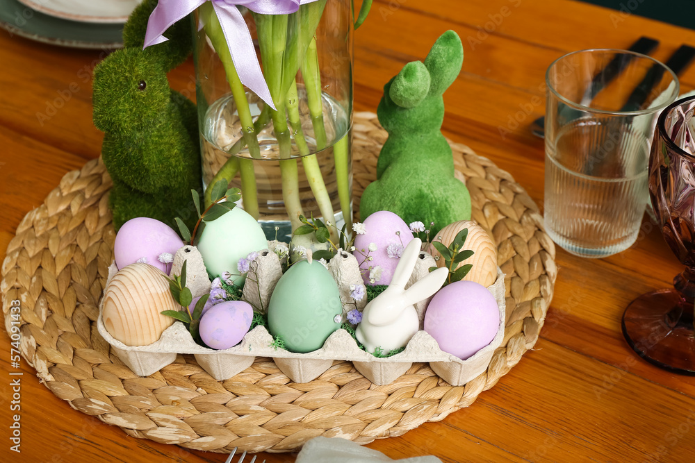Package with Easter eggs, gypsophila flowers and bunnies on wicker mat, closeup