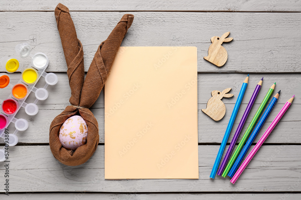 Blank card with Easter egg, paints, rabbits and pens on wooden background