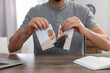 Man ripping photo at table indoors, closeup. Divorce concept