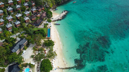 Aerial view of beautiful wooden bungalows in tropical rainforest overlooking white sand beach and turquoise waters of Andaman Sea, Phi Phi, Krabi, Thailand