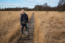 Woman With Dog Walking Wooden Plank Path Through A Peat Bog