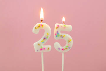 burning white birthday candles on pink background, number 25