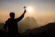 © Tinnakorn - Silhouette of Young man  praying and holding christian cross for worshipping God at sunset background. Christian Religion concept background.