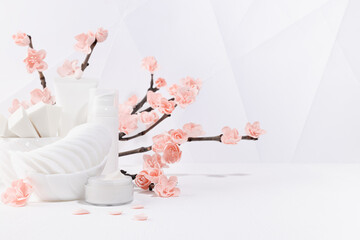 Wall Mural - Cosmetic products for makeup, cleansing skin in white bottles, branch of spring pink sakura flowers, petals, toiletry, elegant light bathroom interior in geometric futuristic asian style, copy space.