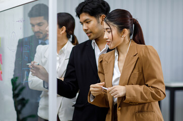 Millennial Asian professional businesswoman employee staff officer in formal business suit standing crossed arms with male female colleagues listening to Indian businessman discussing on glass board