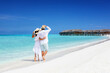 © moofushi - Happy couple in white clothing and with hats walks down a tropical beach with turquoise sea in the Maldives islands