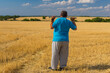 Senior famer with walking pole on the neck standing on harvested wheat field in Ukraine and watching around
