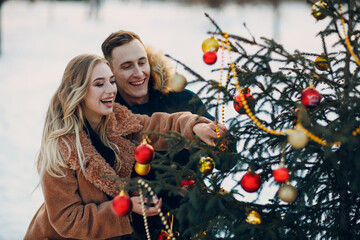 Young adult couple decorates christmas tree in winter park wood fir forest. New year pine holiday party celebration concept.