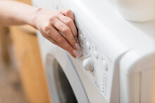 Cropped View Of Woman Pushing Button Of Washing Machine At Home.