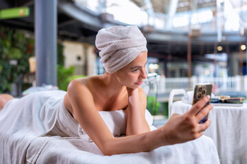 Wall Mural - Young woman lying down on massage bed at wellness center check mobile phone social media network