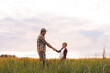© Acronym - Farmer and his son in front of a sunset agricultural landscape. Man and a boy in a countryside field. Fatherhood, country life, farming and country lifestyle concept.