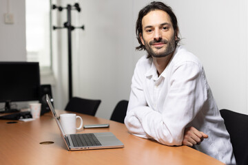 Wall Mural - portrait d'un jeune homme souriant, employé de bureau assis devant son ordinateur au bureau.