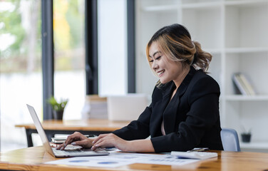 Portrait of attractive young business woman working with laptop and documents on office desk.