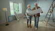 © kinomaster - Elderly man and woman are looking through sheet with plan of an apartment and discussing renovation project. Aged couple is planning improvement of their home. Concept of repair, decoration, interior