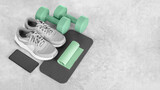 Fototapeta Sypialnia - Fitness equipment on a gray concrete background. Sports shoes, smartphone, dumbbells, mat, exercise band, copy space. Fitness and activity. Smart fitness training. Home workout online. 