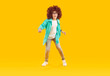 Happy smiling preteen boy in curly red wig dancing. Excited boy wearing glasses, shirt, jeans and sneakers having fun over yellow studio background. Positive emotions concept