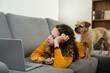 © Oksana Klymenko - Favorite hobby. Teen girl is watching a movie on a laptop and is lying on the couch at home with dog pet.