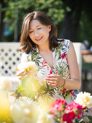 Wall Mural - Woman is admiring of blooming roses in public park. Summer vibes. Tropical plants and flowers in bloom in garden. Floriculture as hobby.