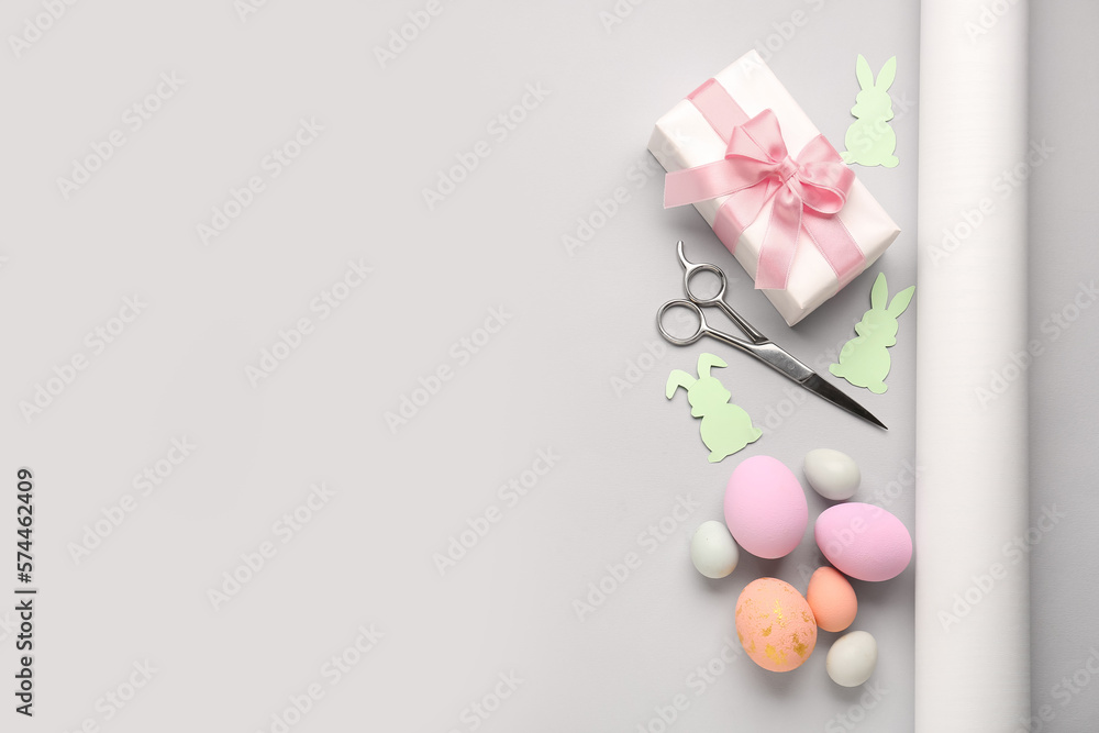Gift with Easter eggs, scissors and paper rabbits on grey background