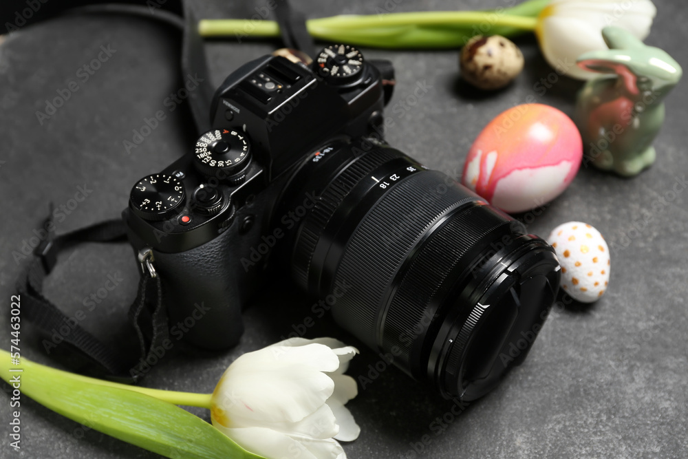 Professional photo camera, tulips and Easter eggs on dark background, closeup