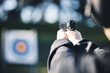 © Azee Jacobs/peopleimages.com - Gun, target and person training outdoor for shooting range, game exercise or sports event closeup. Hands with firearm and circle for aim, vision and practice, police learning academy or field gaming