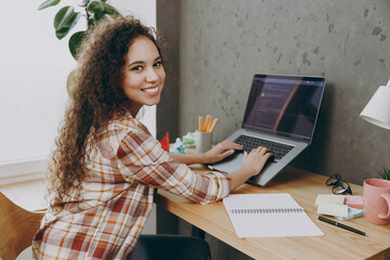 Side view young fun programmer student smart successful employee IT business woman of African American ethnicity wearing casual shirt sit working at office desk with laptop pc computer coding indoors.