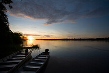 Two Boats Sit At The Shore Of The Amazon River In Peru At Sunset.