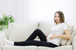 © Andrii - Facial expression of pregnant woman on white sofa.
