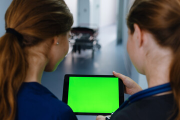 A view from the back of two female doctors who are looking at a tablet screen with a green screen. Chromakey.