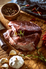 Wall Mural - Two beef steaks on a butcher board surrounded by spices, herbs and garlic, next to a meat cleaver