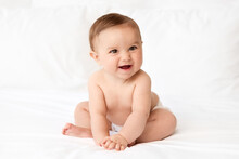 Happy Baby Sitting On White Bed Leaning On Hands