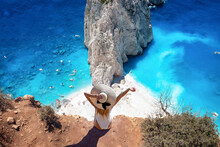 A Tourist Woman Sits At The Viewpoint Of Keri And Enjoys The View Of The Famous Mizithres Rocks With Turquoise Sea At Zakynthos Island, Greece