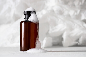 Brown bottle with foam at white texture background. Shampoo, body or facial cleanser cosmetic concept