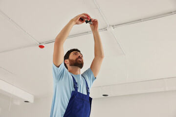 Poster - Electrician with pliers repairing ceiling wiring indoors