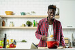 © JustLife - African man cooking in modern kitchen. Handsome chef preparing food.