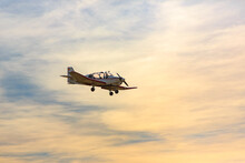 Single-engine Airplane Flies Against The Backdrop Of Sunset And The Woman Pilot Waves Her Hand.