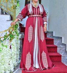 Wall Mural - A Moroccan woman wearing a red kaftan is standing on the stairs