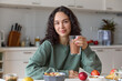 Smiling Young Woman Enjoying a Healthy Meal at Home. A young adult woman with long brown hair is smiling and holding a glass of smoothie in her domestic kitchen. Healthy food concept. 