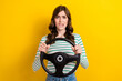 Photo portrait of pretty young girl bite lips nervous hold car rudder dressed stylish striped outfit isolated on yellow color background