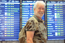 Smiling Old Senior Man In Airport With Luggages Waiting For His Flight Departure Gate. Traveler Concept People With Backpack And Suitcases.