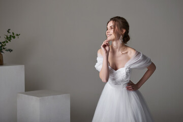 A beautiful young bride model in long lace dress in minimalist white studio interior. Wedding photography.