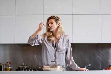 Wall Mural - Girl with cooking pot, doing housework. Housekeeping concept. Beautiful woman stands near table on kitchen at home. Housewife cooking on the kitchen in the morning.