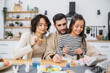 © LIGHTFIELD STUDIOS - Parents and smiling kid holding paintbrushes near Easter eggs in kitchen.