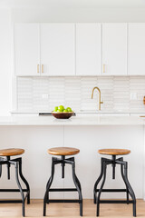 Wall Mural - A kitchen detail with white cabinets, a picket tiled backsplash, gold faucet and hardware, and bar stools sitting at the marble island.