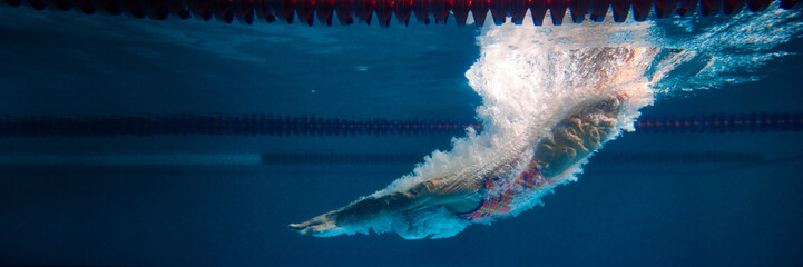 Diving into water. Professional female swimmer training in swimming pool indoor. Underwater view. Concept of sport, endurance, competition, energy, healthy lifestyle. Banner. Space for ad, text