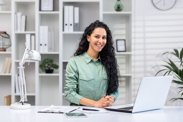 Wall Mural - Portrait of successful beautiful business woman, Hispanic woman in home office smiling and looking at camera, woman at work with laptop typing on keyboard.