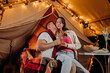 © bondvit - Happy lovely couple relaxing in glamping on summer evening and drinking wine near cozy bonfire. Luxury camping tent for outdoor recreation and recreation. Lifestyle concept